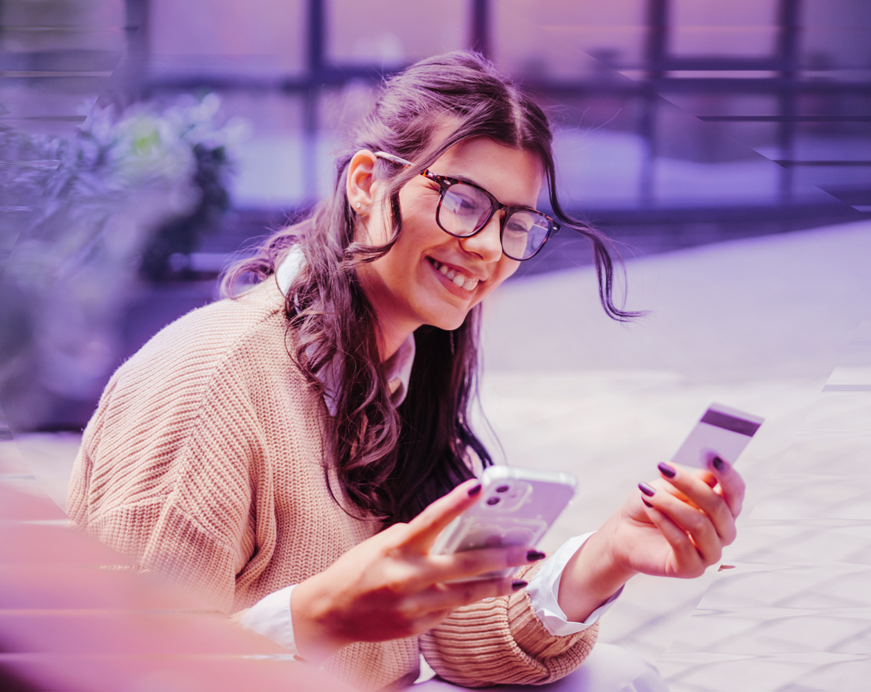 Image of a happy woman using her credit card and her phone.