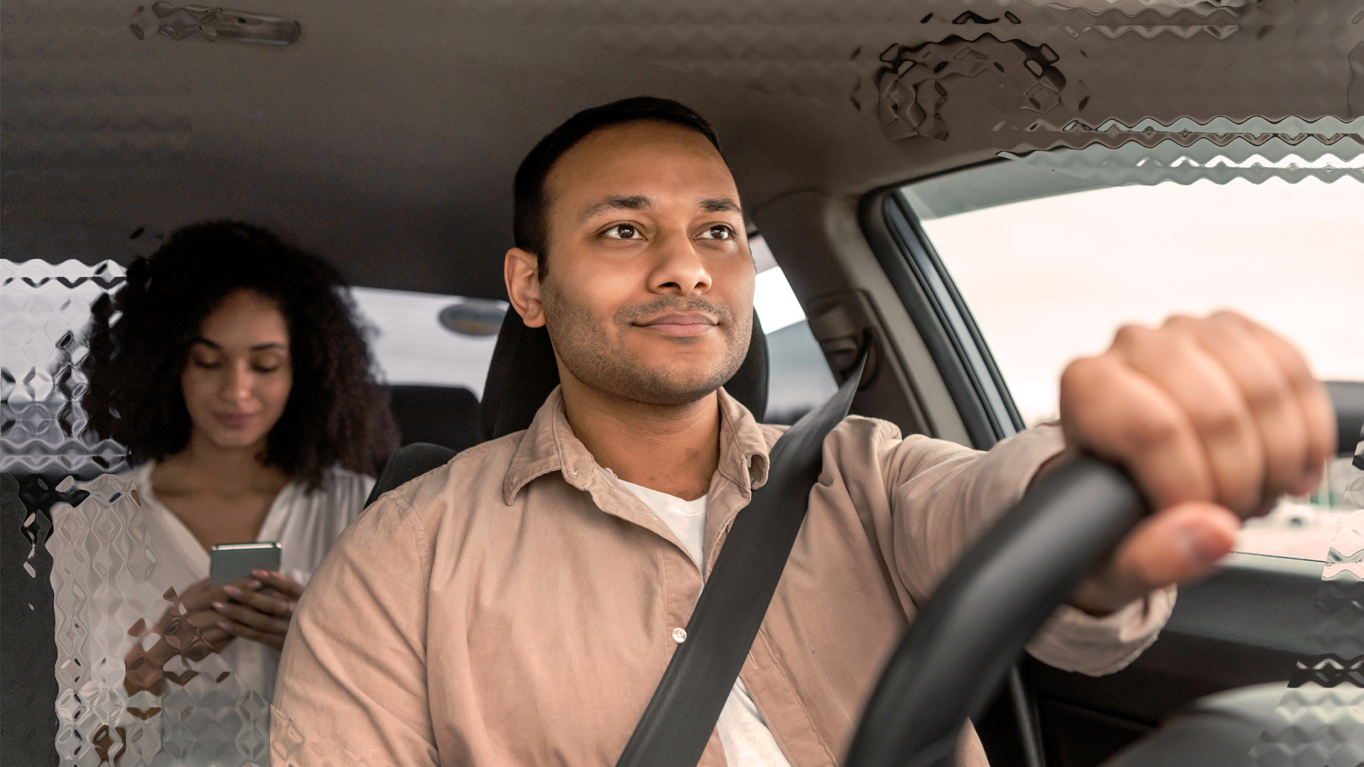 Image of a man driving a ride share car with a passenger at the back.